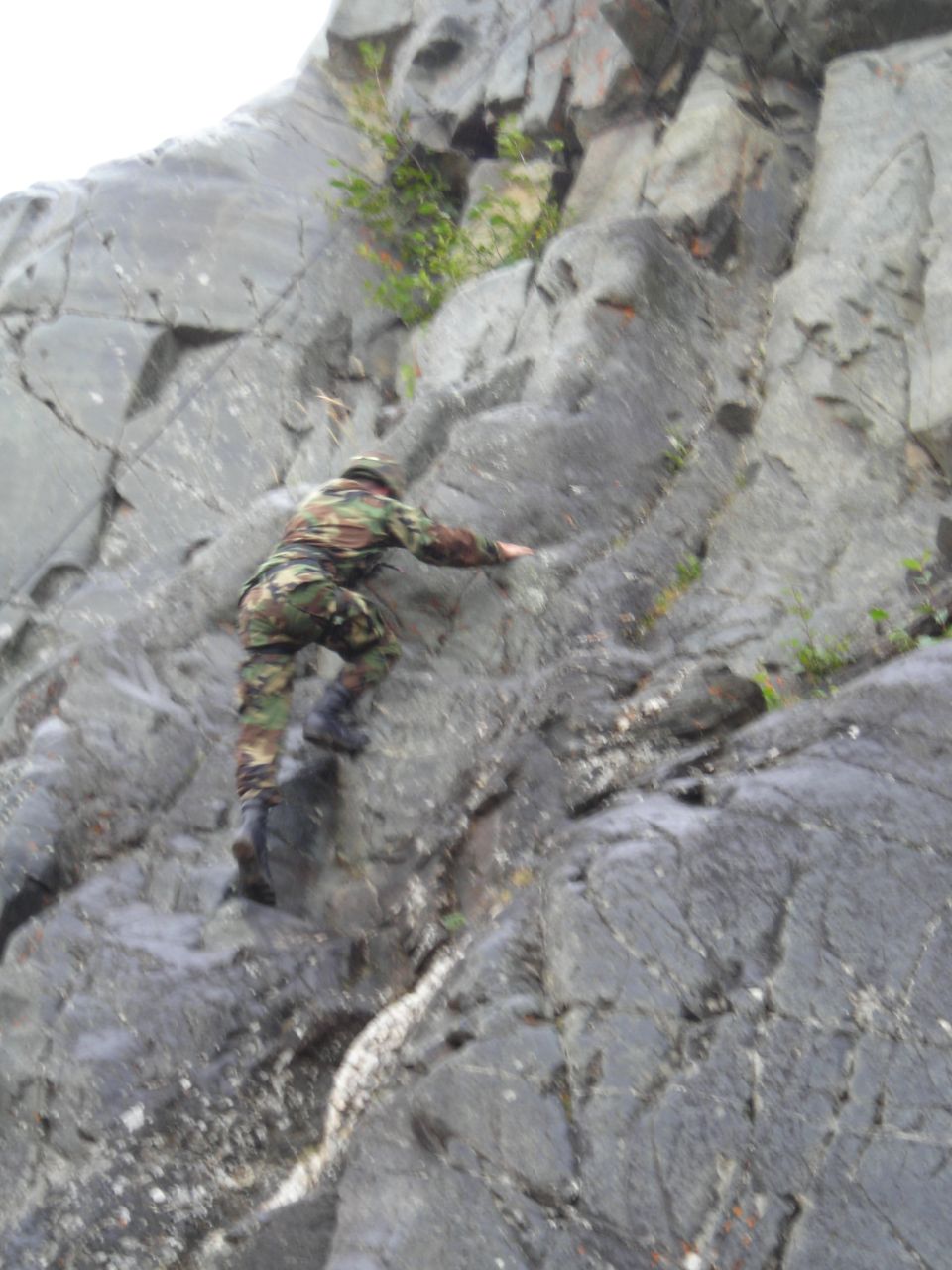 person in camouflage climbing a rocky cliff