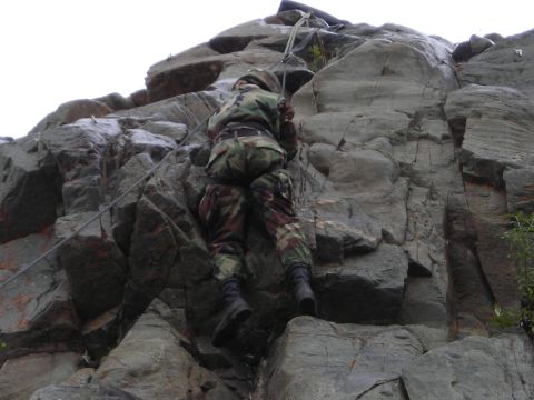 2003 Jeep TJ - A soldier in camouflage gear ascends a steep, rocky cliff face, utilizing ropes for assistance.