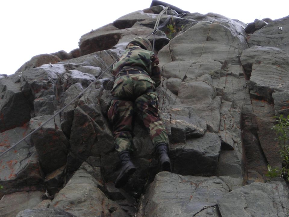 Soldier in camouflage climbing a rocky cliff face with ropes