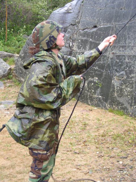 2003 Jeep TJ - A person in camouflage gear is rappelling down a large rock face using a rope.