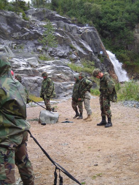 2003 Jeep TJ - Military personnel gather near a waterfall on a rocky incline, with one soldier holding a rope in the foreground.
