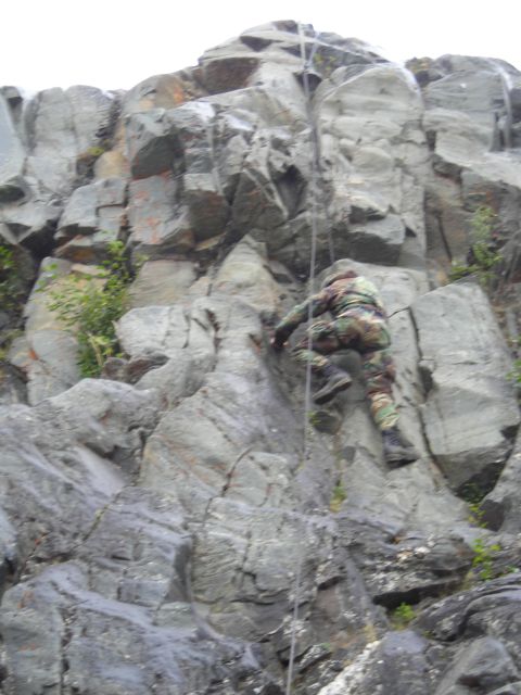 2003 Jeep TJ - A person in camouflage gear is rappelling down a large, rocky cliff face.