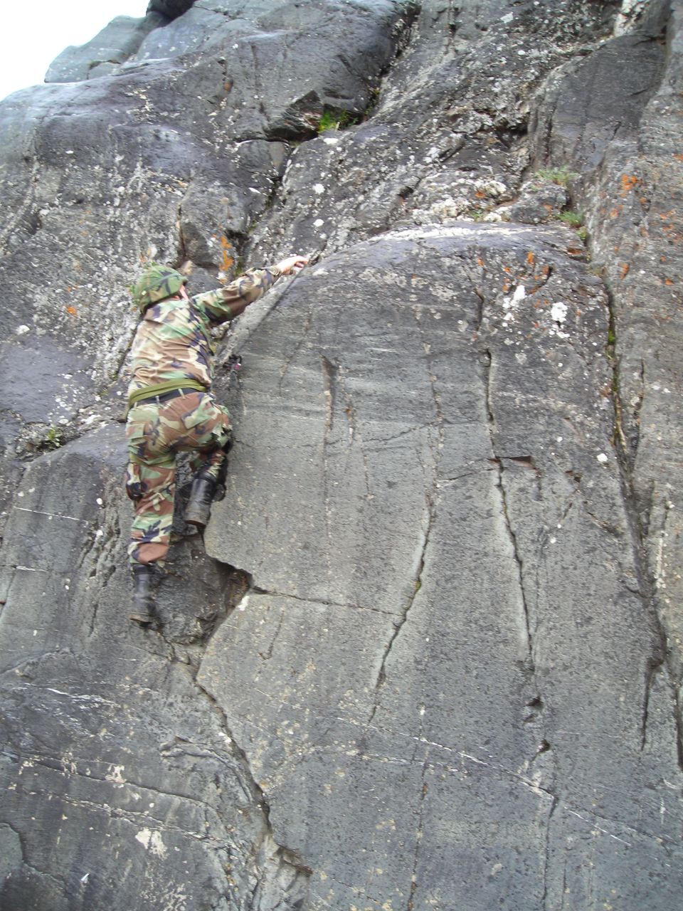 Person in camouflage climbing up a rocky cliff face