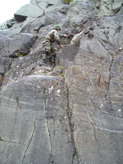 2003 Jeep TJ - A person in military-style camouflage gear ascends a challenging, textured rock formation.