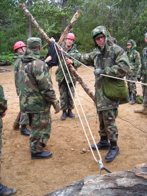 2003 Jeep TJ - Soldiers in camouflage uniforms engage in a training exercise involving ropes and wooden logs, with some wearing protective helmets.