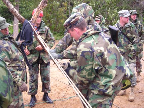 2003 Jeep TJ - A group of soldiers in camouflage uniforms appear to be engaged in some form of training exercise involving ropes and a wooden frame.
