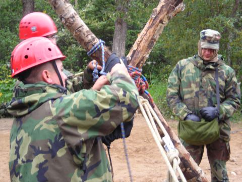 2003 Jeep TJ - Individuals in camouflage gear and helmets are engaged in rope knot tying practice outdoors.
