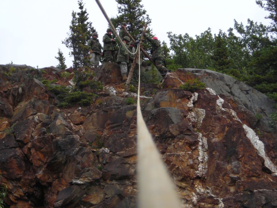 Military personnel rappelling down a rocky cliff face