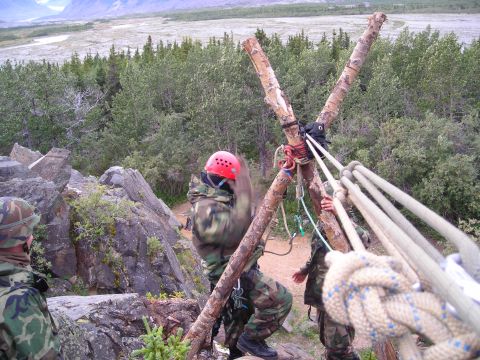 2003 Jeep TJ - People are setting up ropes on a wooden tripod structure on a rocky outcrop with trees and mountains in the background.
