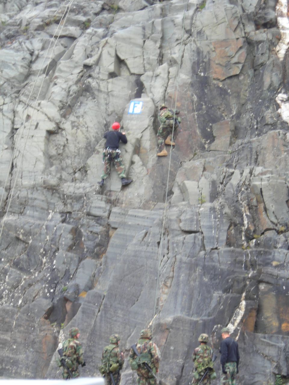 Military personnel rappelling and climbing a rocky cliff face