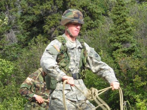 2003 Jeep TJ - Two soldiers in camouflage gear are seen outdoors, one holding ropes, with trees in the background.