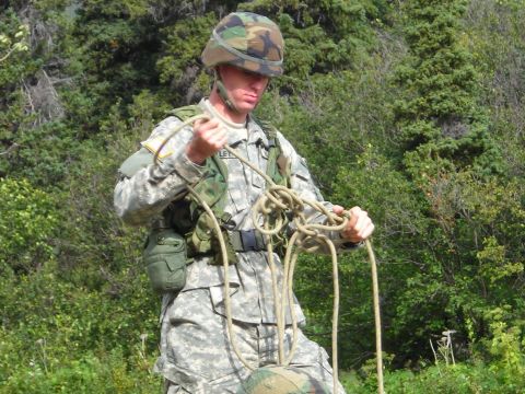 2003 Jeep TJ - A soldier prepares a rope for an activity, with a wooded area behind him.
