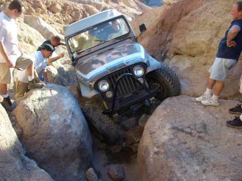 1985 Ford Bronco - A Jeep CJ-7 navigates a rocky off-road trail, with several people observing its progress.