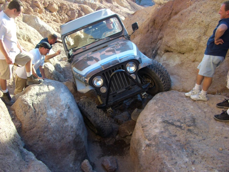 Jeep CJ-7 stuck between rocks, camouflage paint, blue stripe, people watching