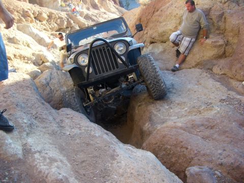 1985 Ford Bronco - A Jeep Wrangler maneuvers through a challenging rocky terrain in a desert canyon.