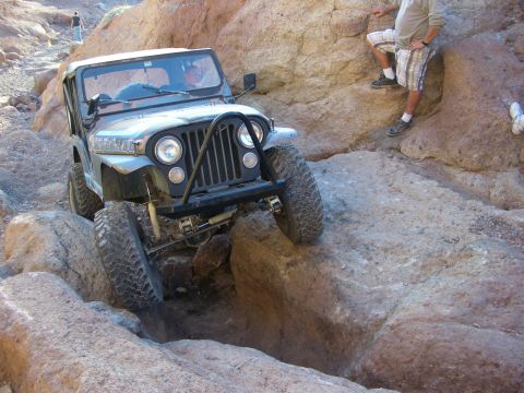 1985 Ford Bronco - A gray Jeep CJ-7 is shown off-roading through a rocky canyon, demonstrating its capability on challenging terrain.