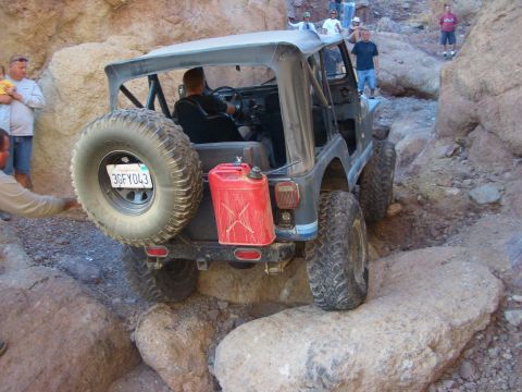 1985 Ford Bronco - A Jeep CJ-7 navigates a narrow, rocky canyon trail with people watching.