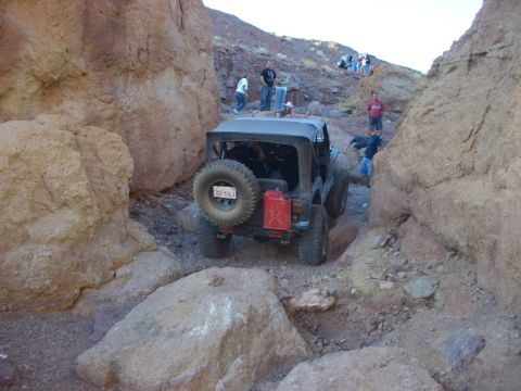 1985 Ford Bronco - A black Jeep Wrangler maneuvers through a narrow, rocky canyon with people watching from the slopes above.