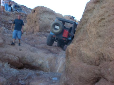 1985 Ford Bronco - A Jeep Wrangler navigates a rocky trail, with people and another vehicle visible in the background.