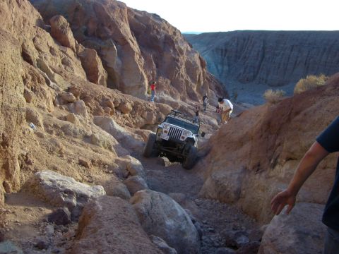 1985 Ford Bronco - A white Jeep Wrangler tackles a challenging rocky terrain in a desert canyon.