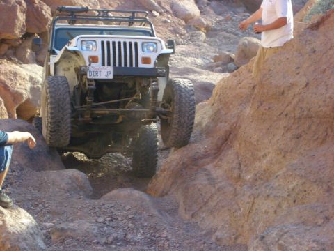 1985 Ford Bronco - A Jeep Wrangler TJ is shown off-roading on a challenging rocky trail, with a person observing from the side.