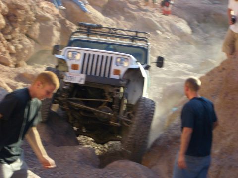 1985 Ford Bronco - A Jeep Wrangler navigates a rocky off-road trail, kicking up dust as it goes.