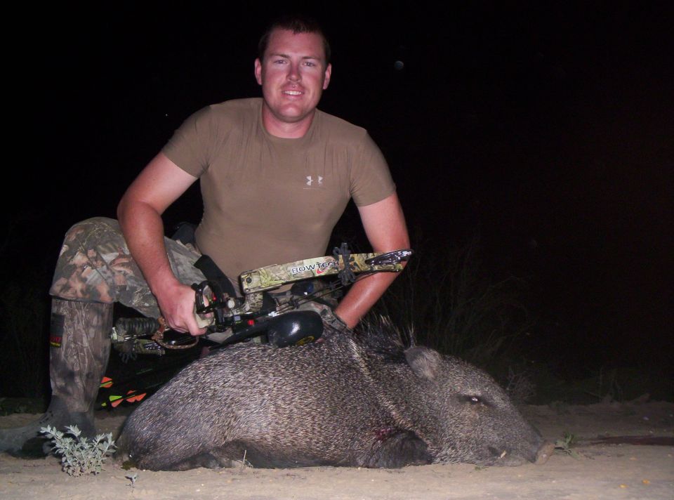 Man with bow and arrow poses with a dead javelina