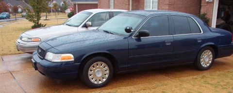 1999 Ford Crown Victoria - Two Ford Crown Victorias are parked side-by-side on a wet driveway.