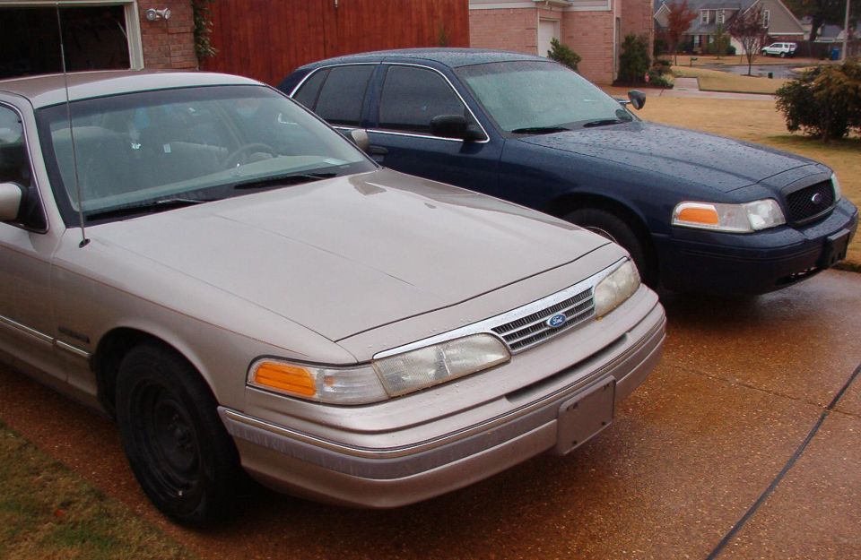 Tan and dark blue Ford Crown Victoria sedans parked front-3/4 in a driveway.