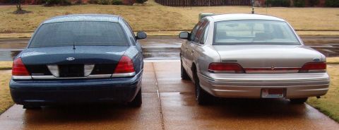 1999 Ford Crown Victoria - Two Ford Crown Victorias, a blue one and a tan one, are parked in a driveway.