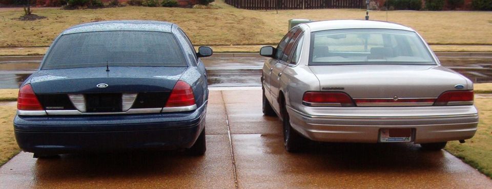 Blue and silver Ford Crown Victoria sedans photographed from the rear on a wet driveway