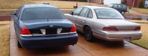 1999 Ford Crown Victoria - Two Ford Crown Victorias are parked side-by-side on a wet driveway.