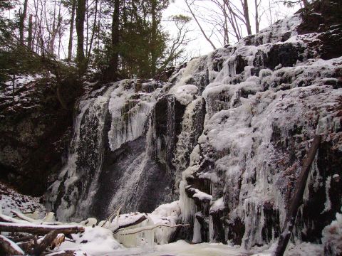 2000 Chevrolet Tahoe - A partially frozen waterfall cascades down a rocky cliff face in a wooded area during winter.