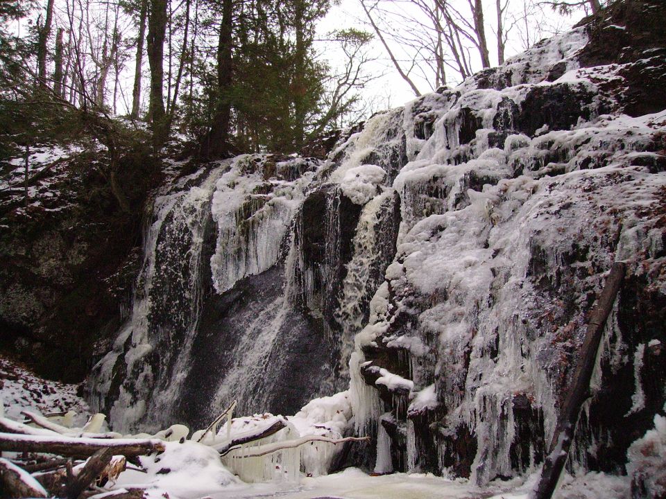 Frozen waterfall with icicles hanging from rocks and trees. Snow on the ground