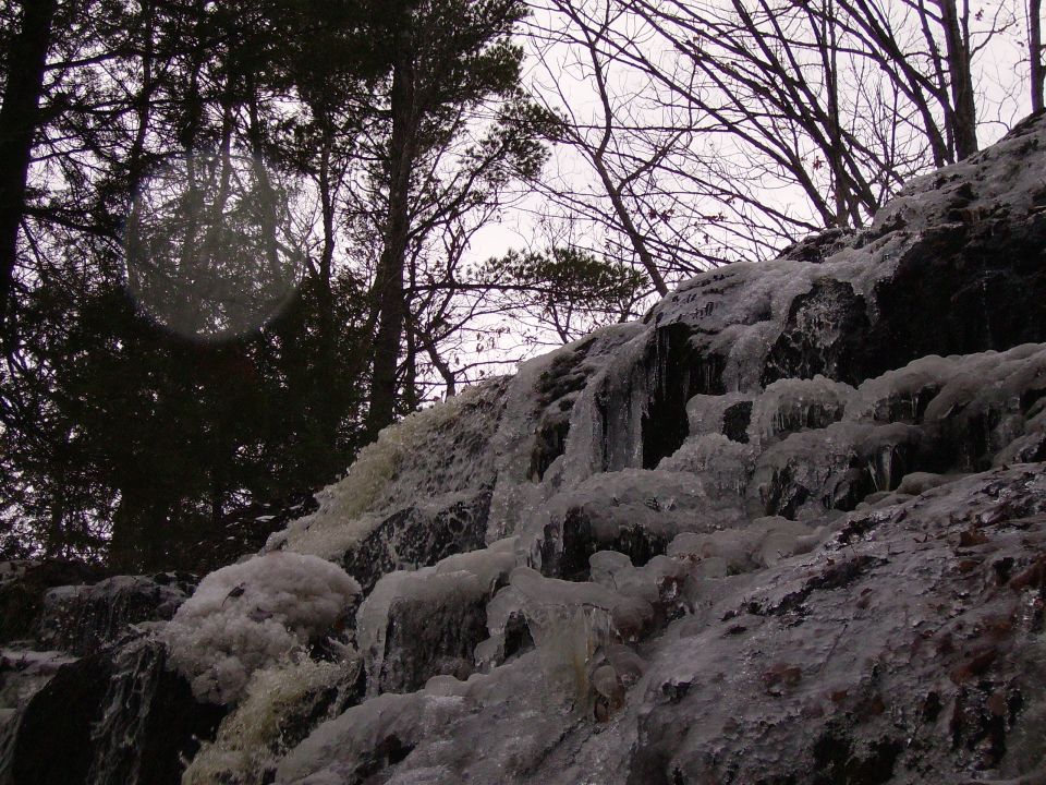 Frozen waterfall cascading down rocks with bare trees in the background