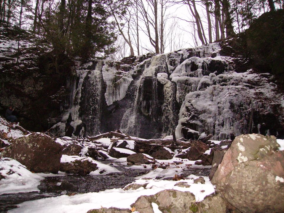 Frozen waterfall with ice and snow. Trees and rocks in foreground