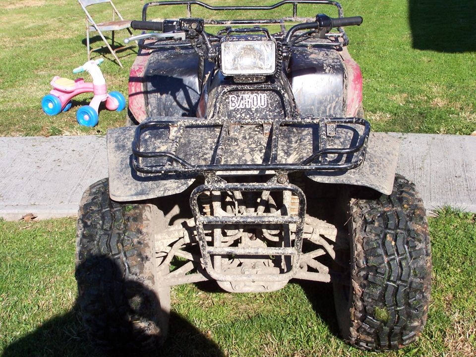 Front view of a muddy Kawasaki Bayou ATV on grass