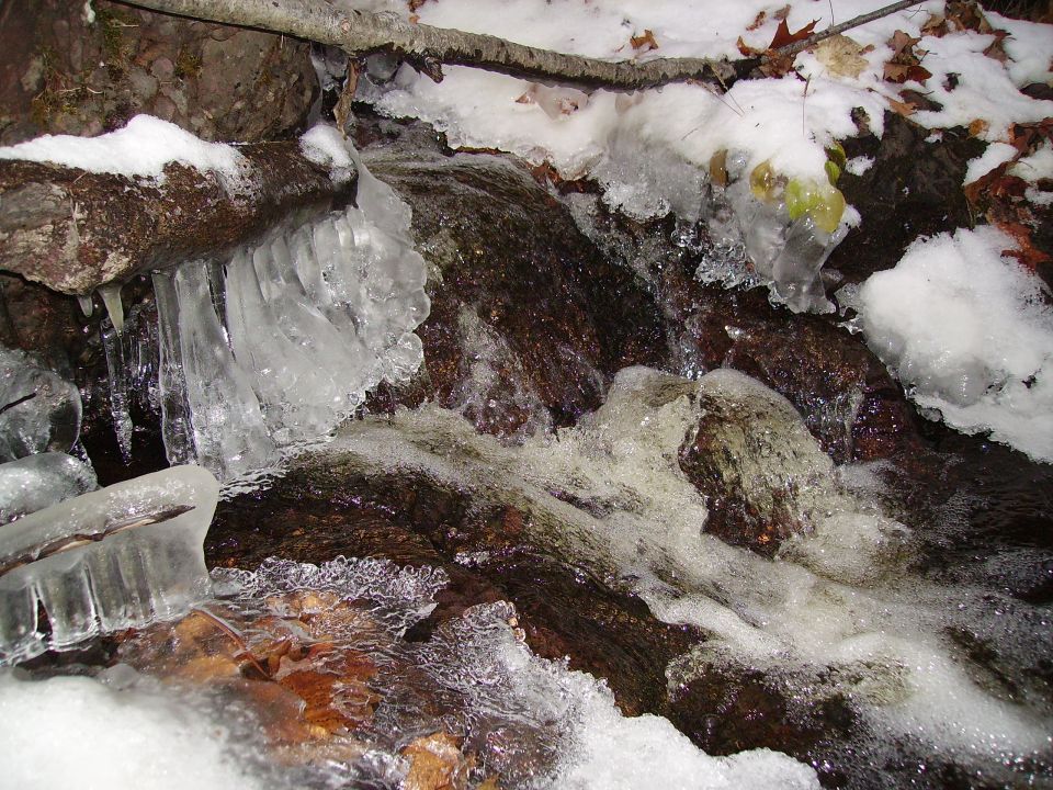 Frozen stream with icicles and snow on rocks and branches