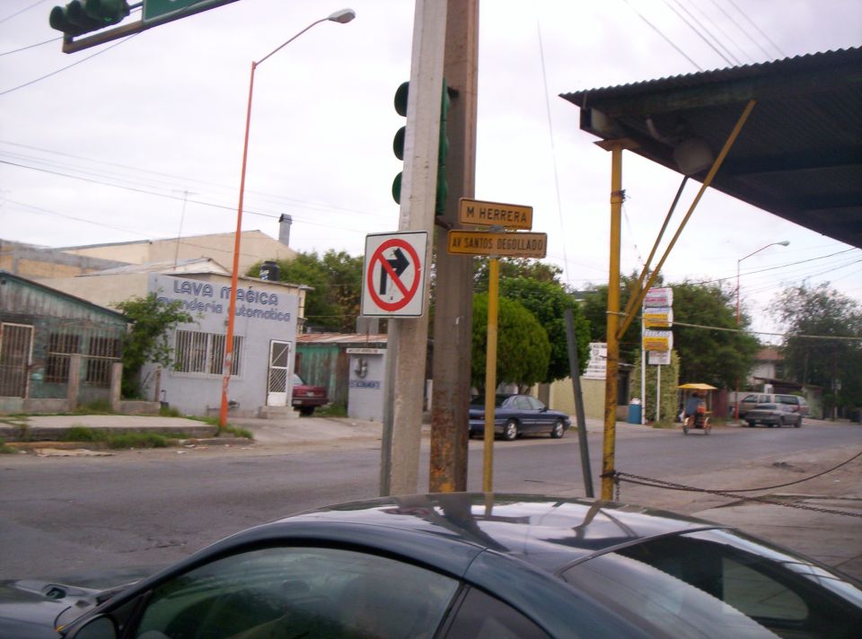 Dark coupe hood and windshield in foreground, street scene with buildings and signs