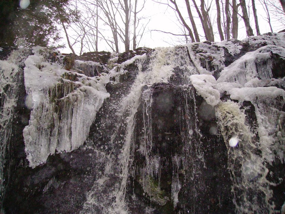 Frozen waterfall with icicles hanging off rocks. Trees are bare in the background