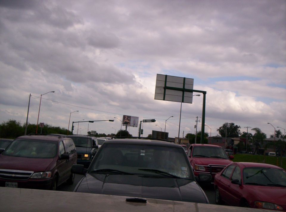Cars stuck in traffic under a cloudy sky. A large sign is visible overhead