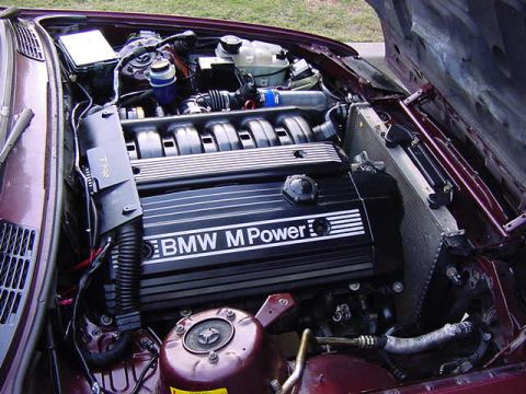 1984 BMW 3 Series - The engine bay of a BMW is shown with the hood open, revealing the engine and M Power engine cover.