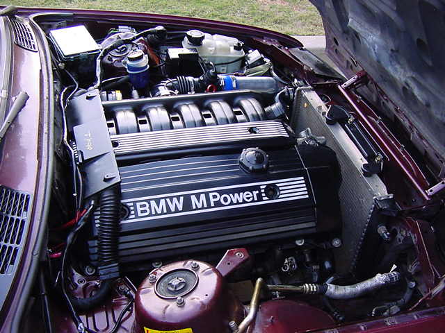 Close-up of a BMW M Power engine bay with the hood open. Shows the engine cover and radiator