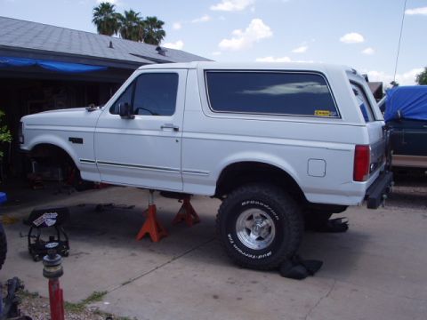 1993 Ford Bronco - A white 1993 Ford Bronco is shown on jack stands, possibly undergoing maintenance or modification.