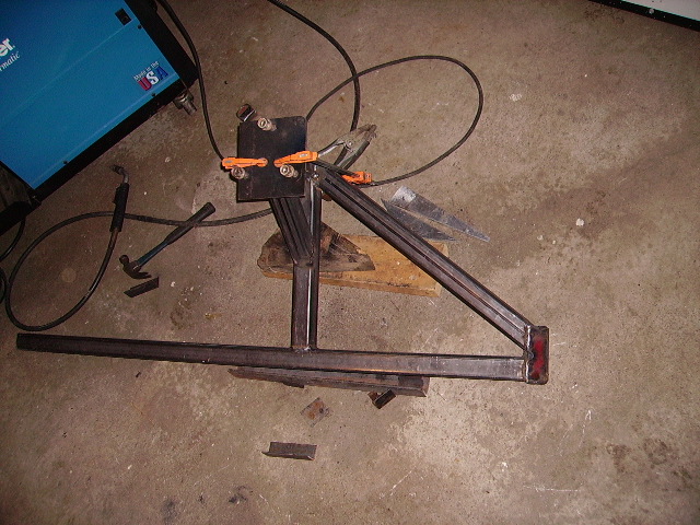 Square-tube swing-out tire carrier arm clamped for welding next to a Miller welder