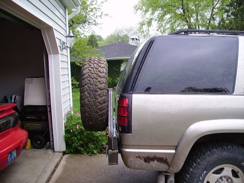 2000 Chevrolet Tahoe - A gold SUV is parked in a driveway next to an open garage, with a spare tire mounted externally on its rear.