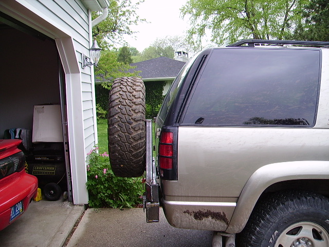Tahoe's steel swing-out tire carrier open with mud-terrain spare beside the rear quarter