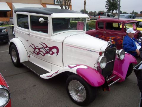 2002 Ford Mustang - A white sedan with purple flames and custom pink fenders is parked next to another hot rod.