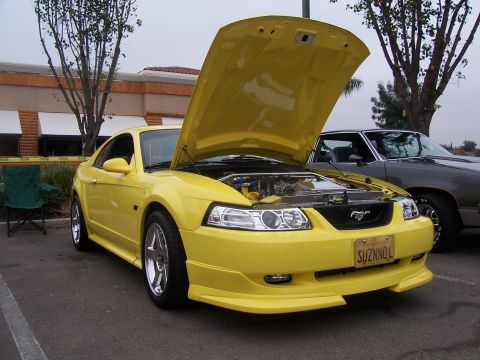 2002 Ford Mustang - A yellow 2002 Ford Mustang is displayed with its hood open, parked outdoors next to another vehicle.
