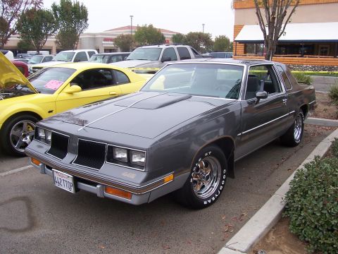 2002 Ford Mustang - A gray 1980s Oldsmobile 442 is parked next to a yellow Ford Mustang.